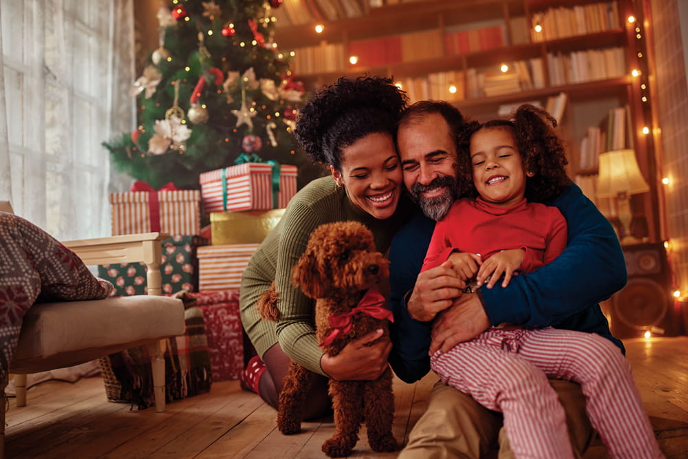 A: three individuals hugging with their dog in front of a Christmas tree